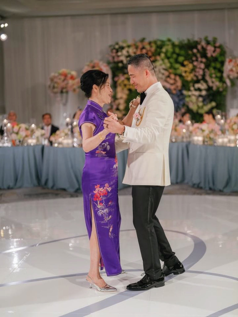  Side view of a mother is wearing a bespoke purple Qipao with trees and sun embroidery to her son's wedding. 