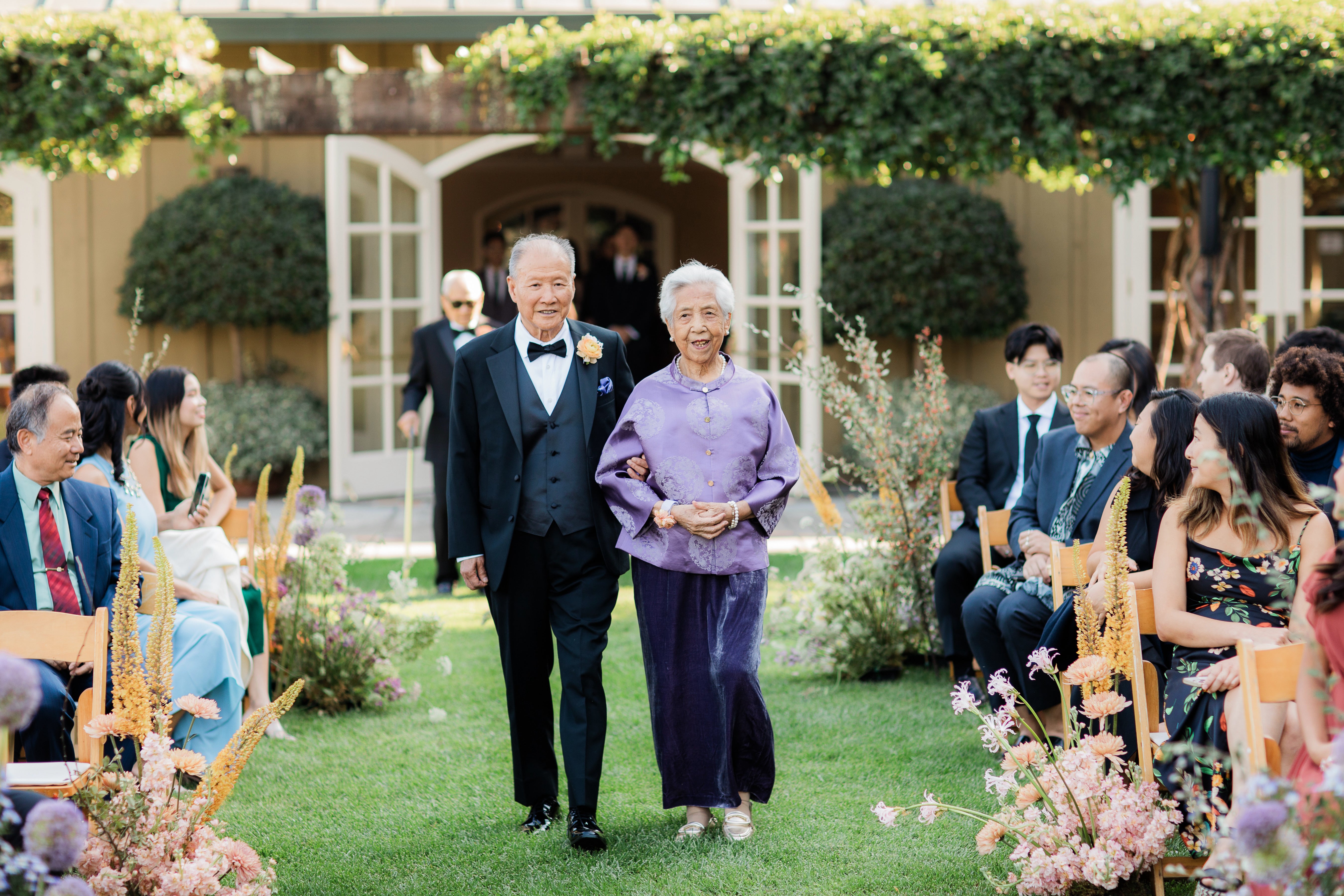 A grandmother wearing a purple tang jacket and a velvet skirt at her grandson's wedding