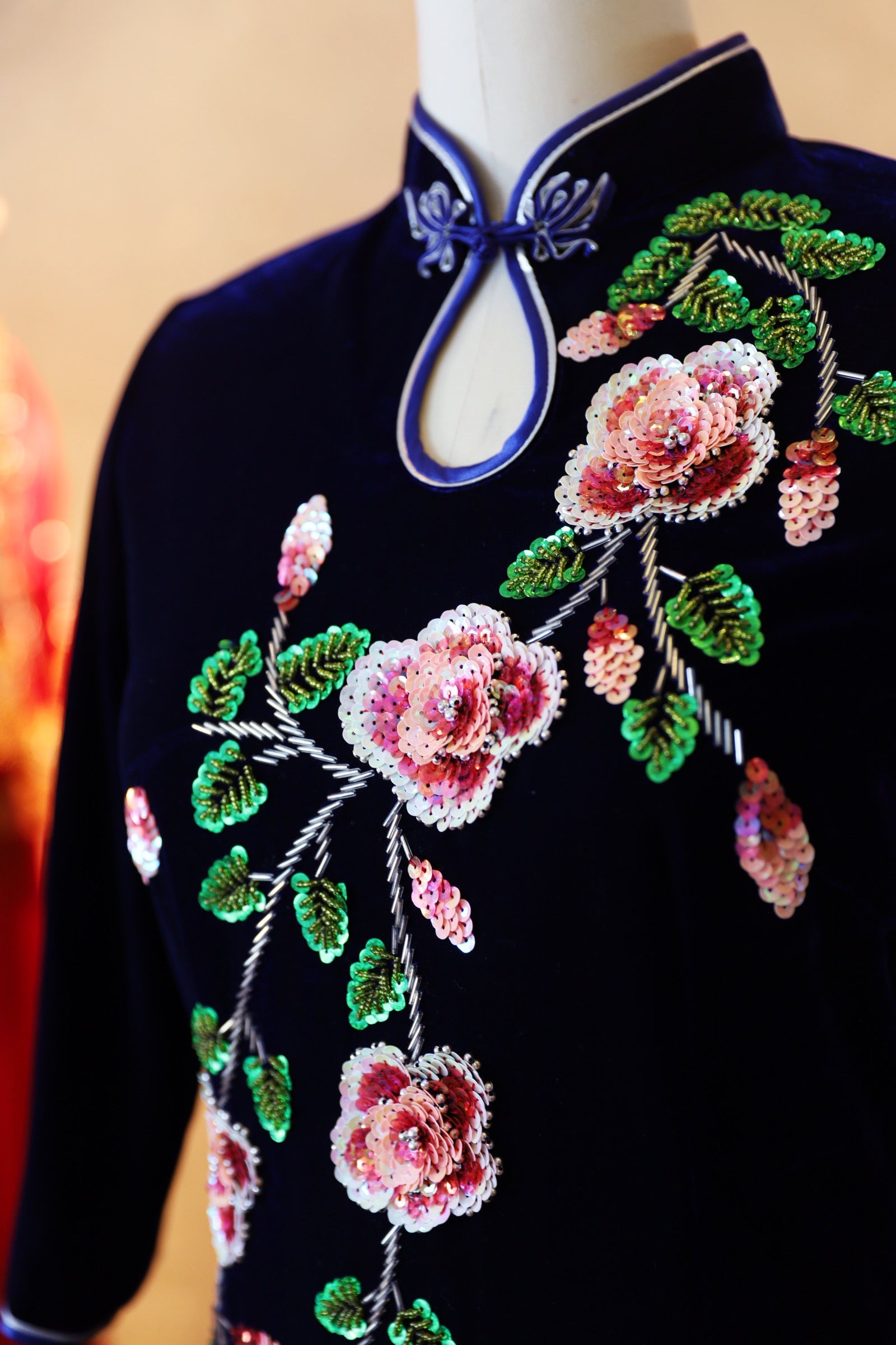 Close-up detail of the hand-beaded peonies on a purple velvet Qipao with a water drop neckline and 3/4 sleeves, designed for mothers during Lunar New Year.