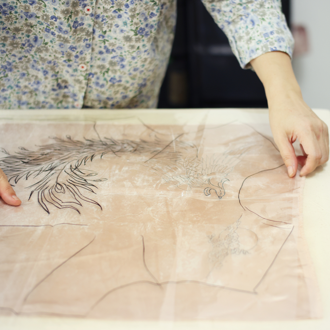 Artisan planning embroidery placement on red silk for a Chinese wedding Qipao