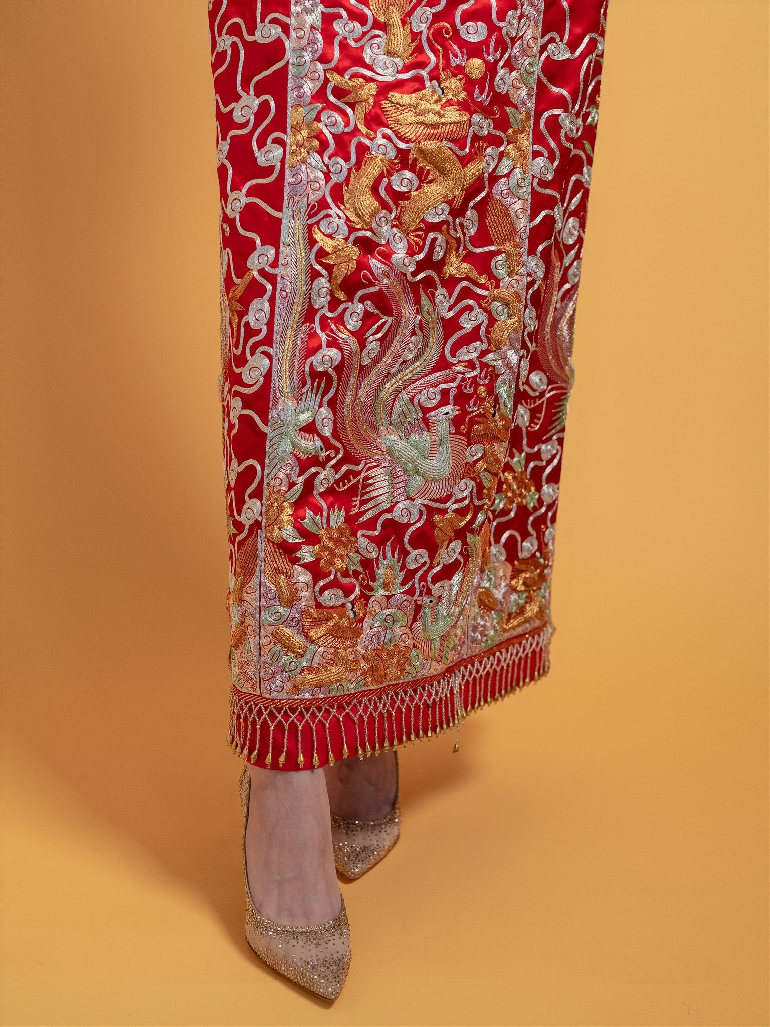 Close-up detail of the 3D hand-embroidered dragon, bat, phoenix, and clouds on a red Chinese Qun Kwa Zhong Wu Fu wedding dress's skirt for traditional tea ceremonies.