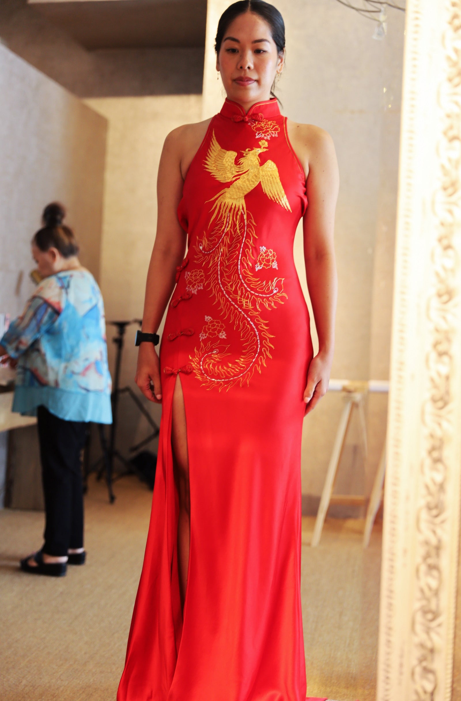 Front view of a bride wearing her modern Cheongsam dress for wedding, featuring halter neckline, gold phoenix embroidery and front slit. 