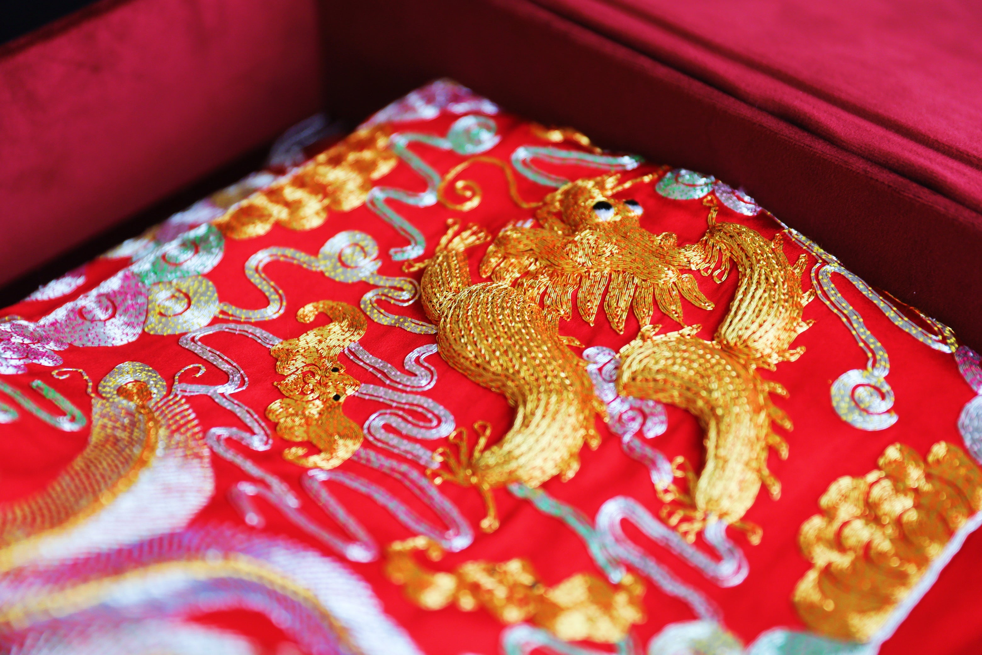 Close up of 3D hand-embroidered dragon, bats, phoenix, and lucky cloud patterns on a red Qun Kwa. 