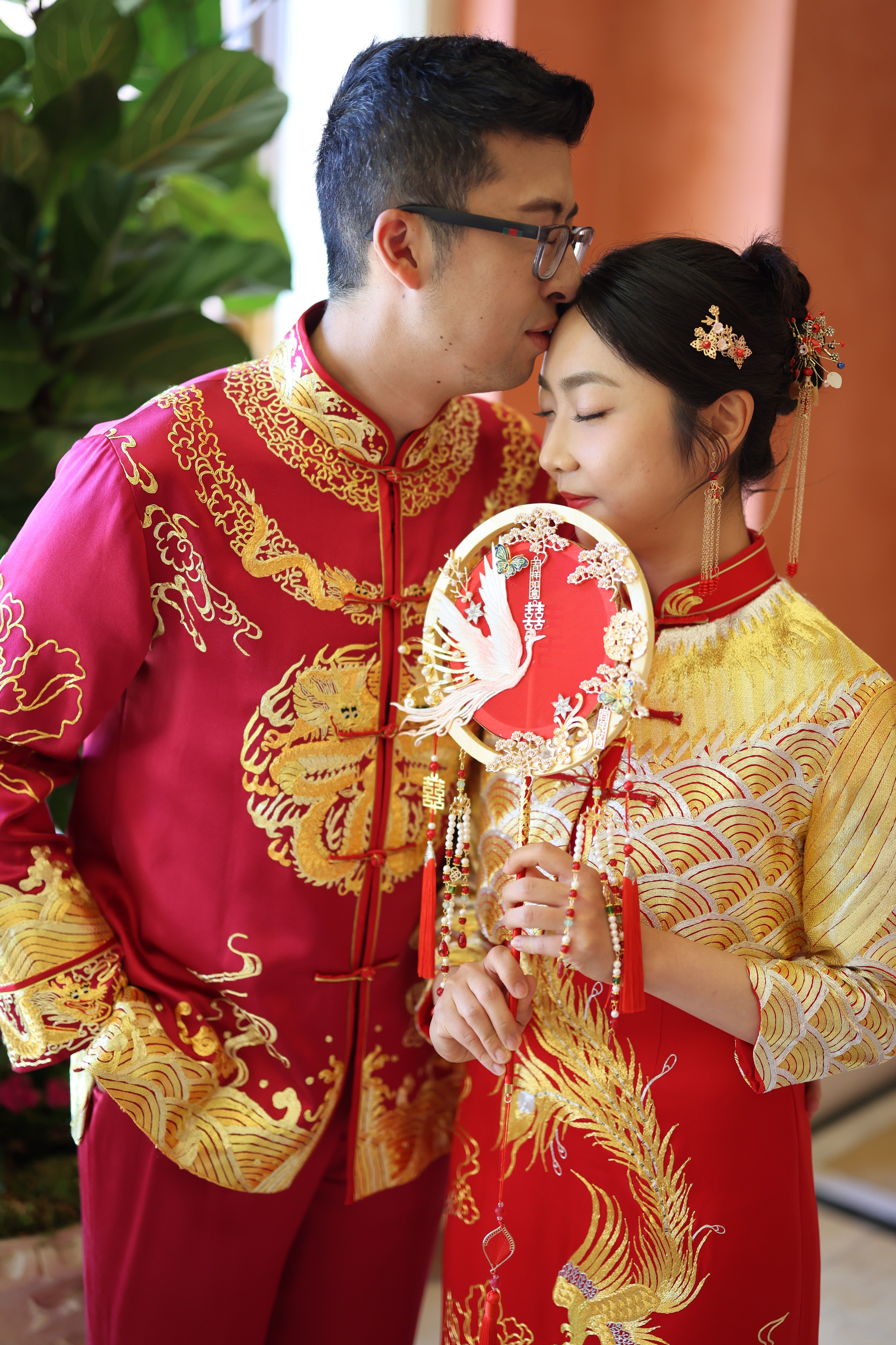 A groom wearing red silk tang suit with gold dragon, cloud and peony embroidery