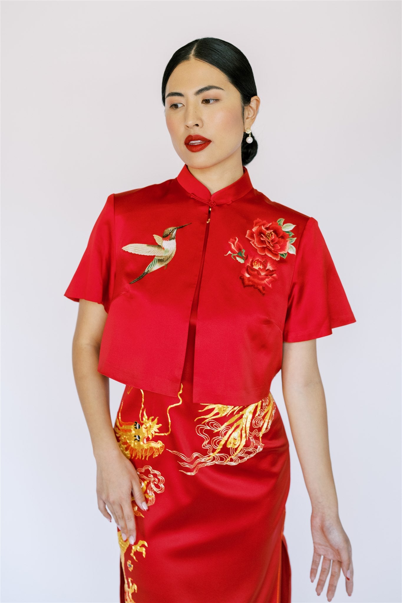 A woman wearing a red wedding Qipao and a short sleeve jacket with bird and rose embroidery