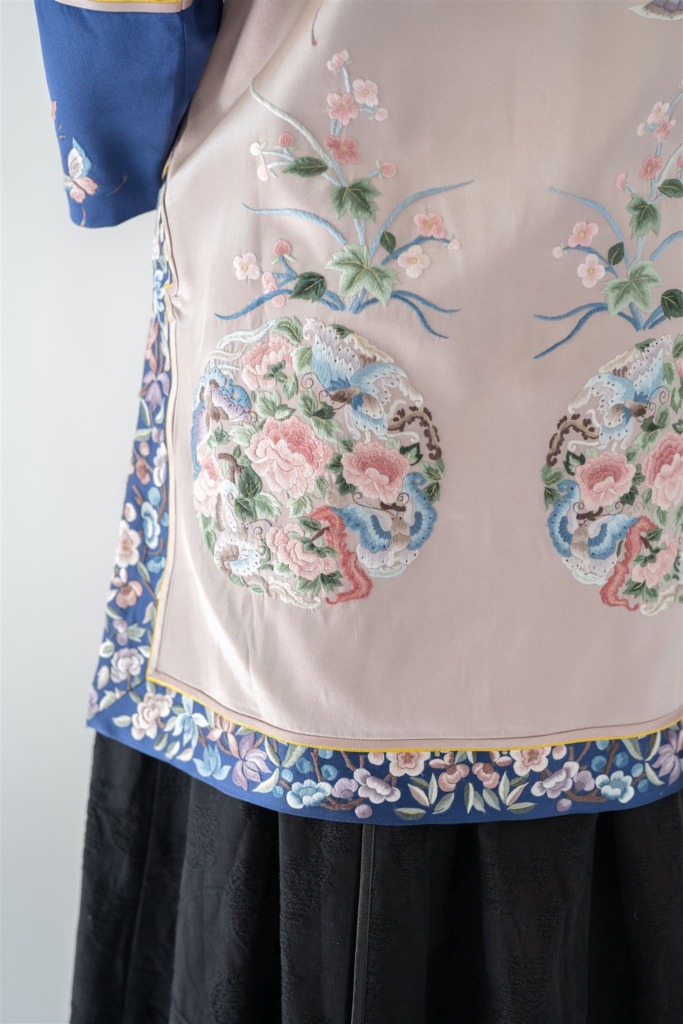 Detail of floral embroidery with peonies, roses, butterflies, and leaves on silver jacket.