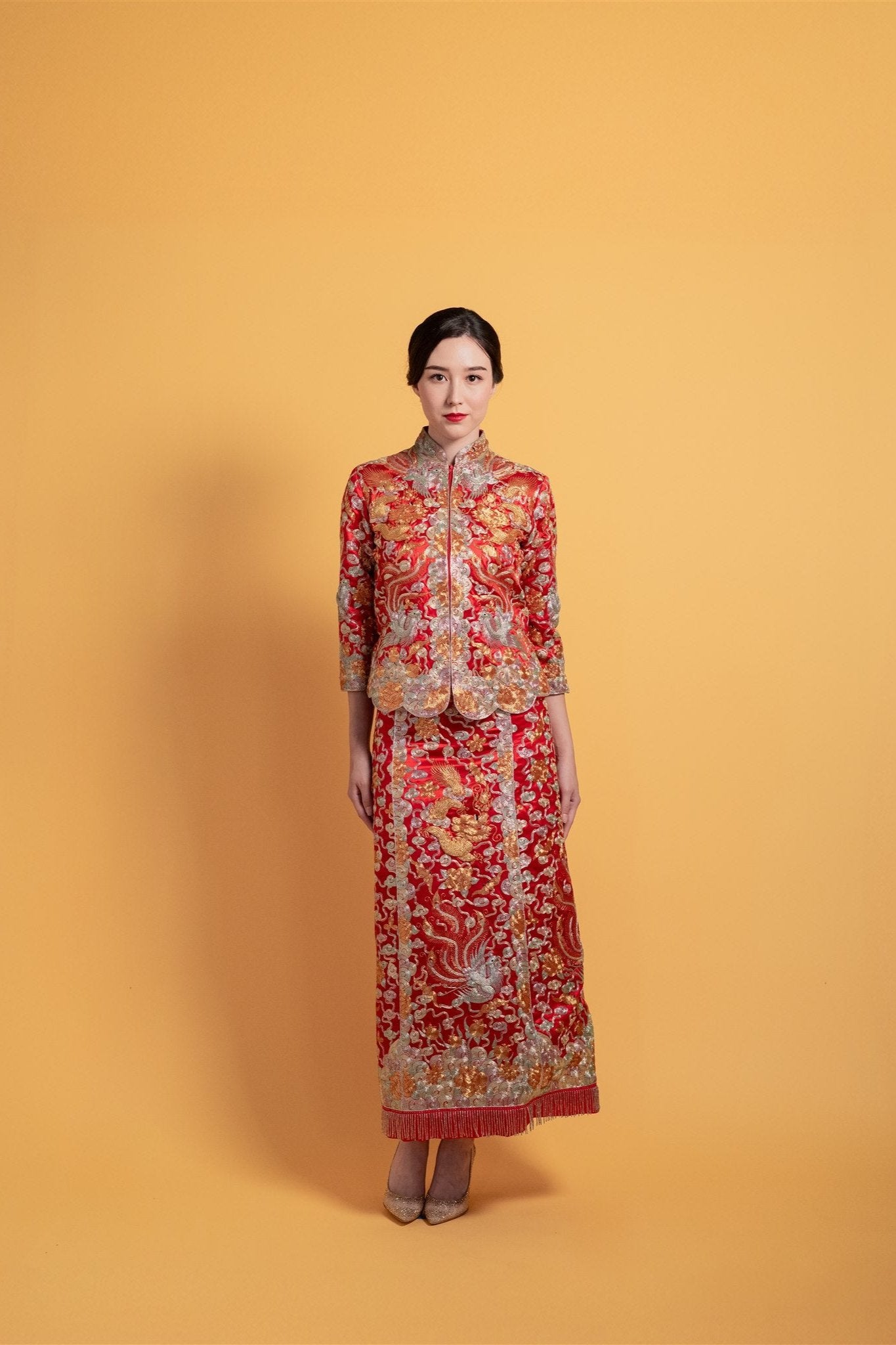 Front view of a bride wearing a red Qun Kwa Da Wu Fu Chinese wedding dress with a fitted top and skirt, showcasing 3D hand-embroidered dragon, phoenix, silver cloud, and peonies, ideal for a traditional tea ceremony.