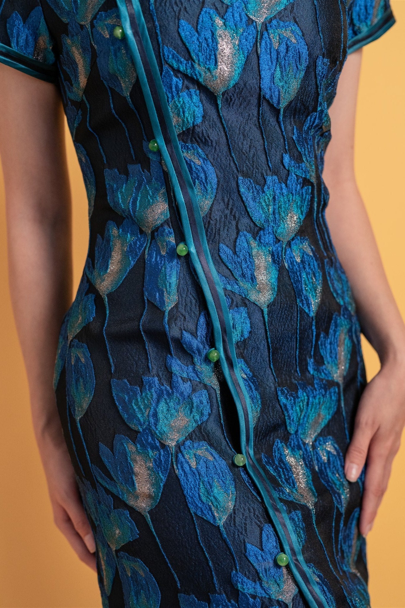 Close-up of tulip silk pattern and green button closure on blue grey cheongsam