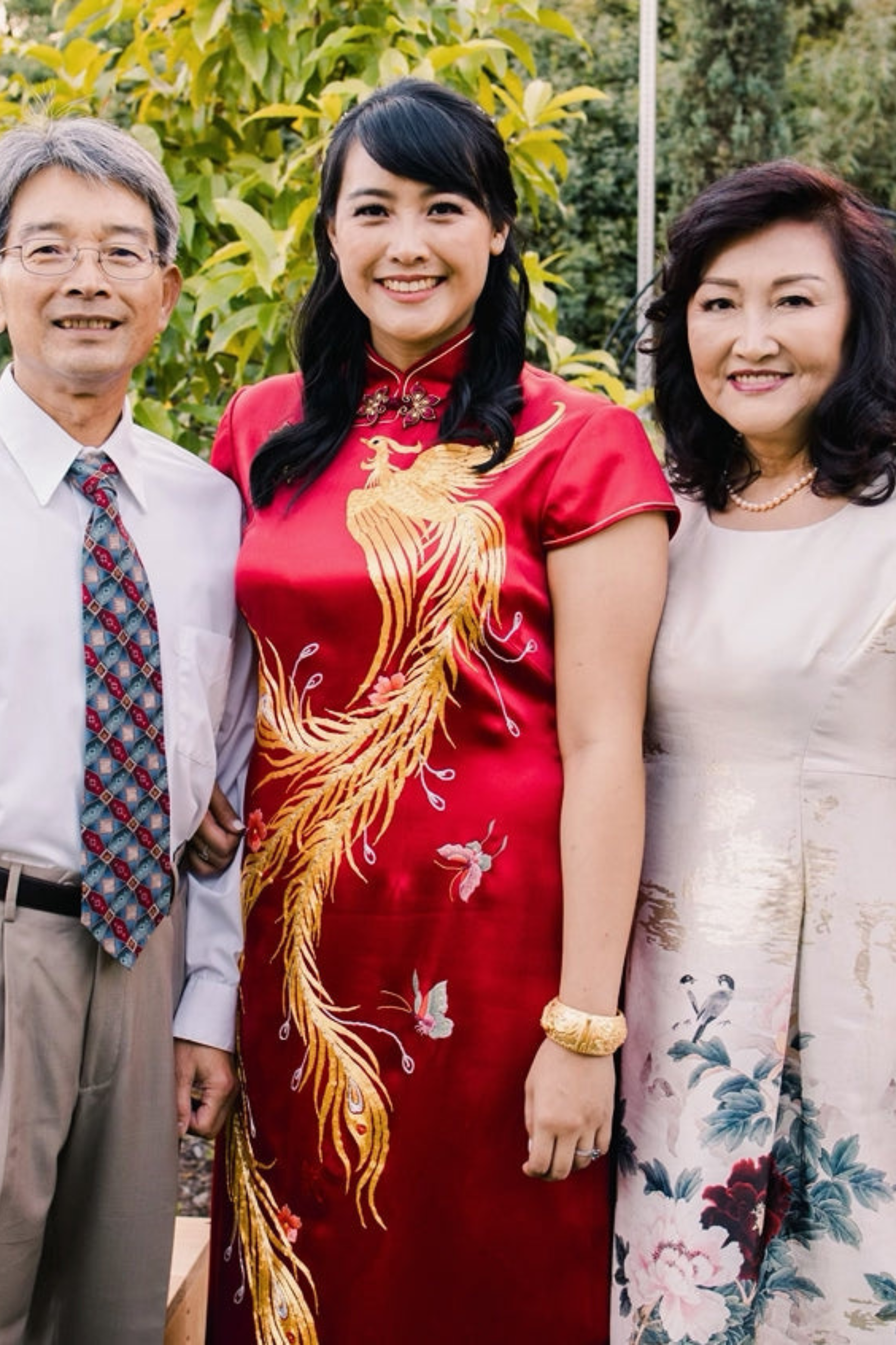 A bride wearing a wine red silk Qipao with gold phoenix, pink butterflies and peonies