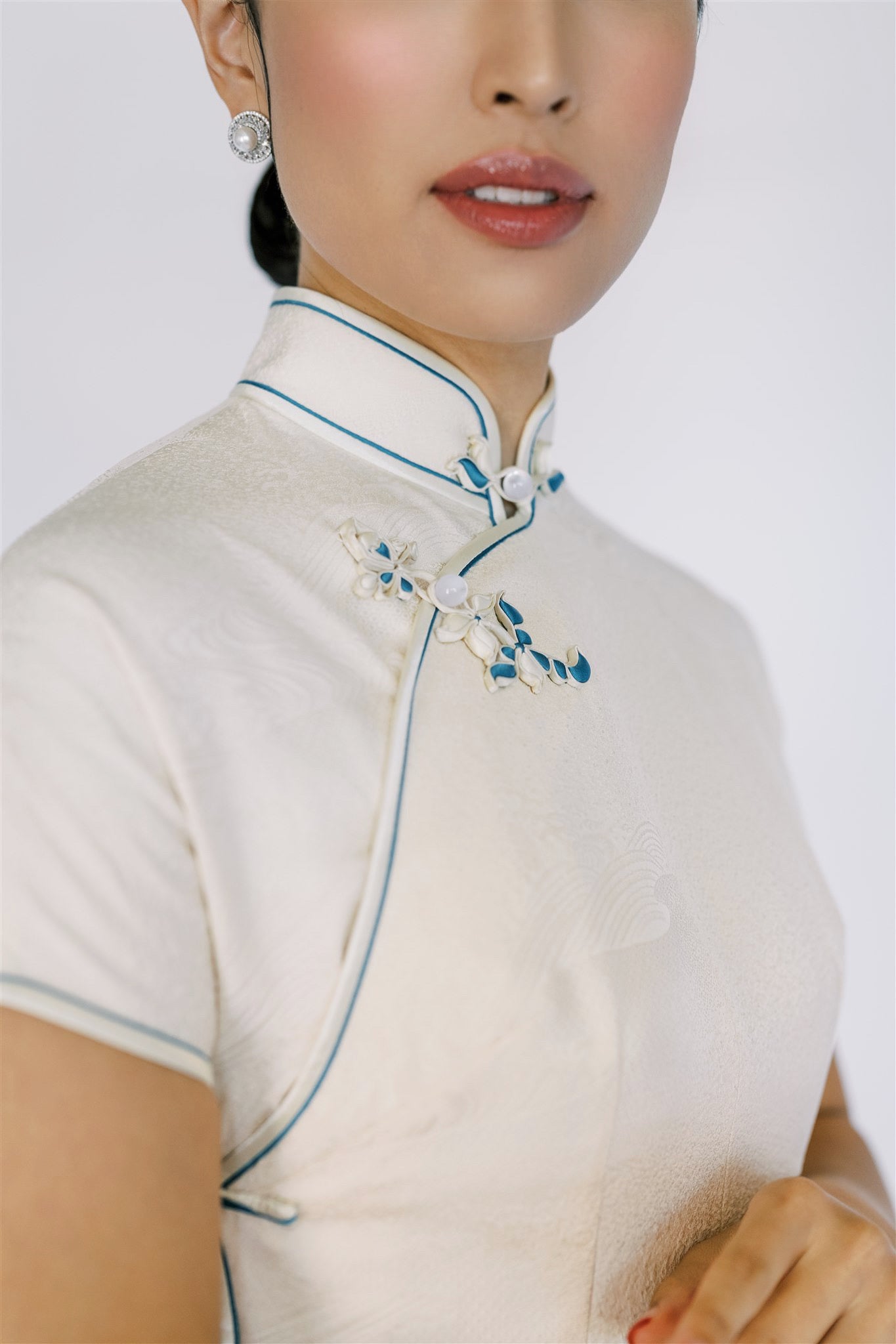 A close up of floral pankou frog knot on a woman wearing white silk Qipao.