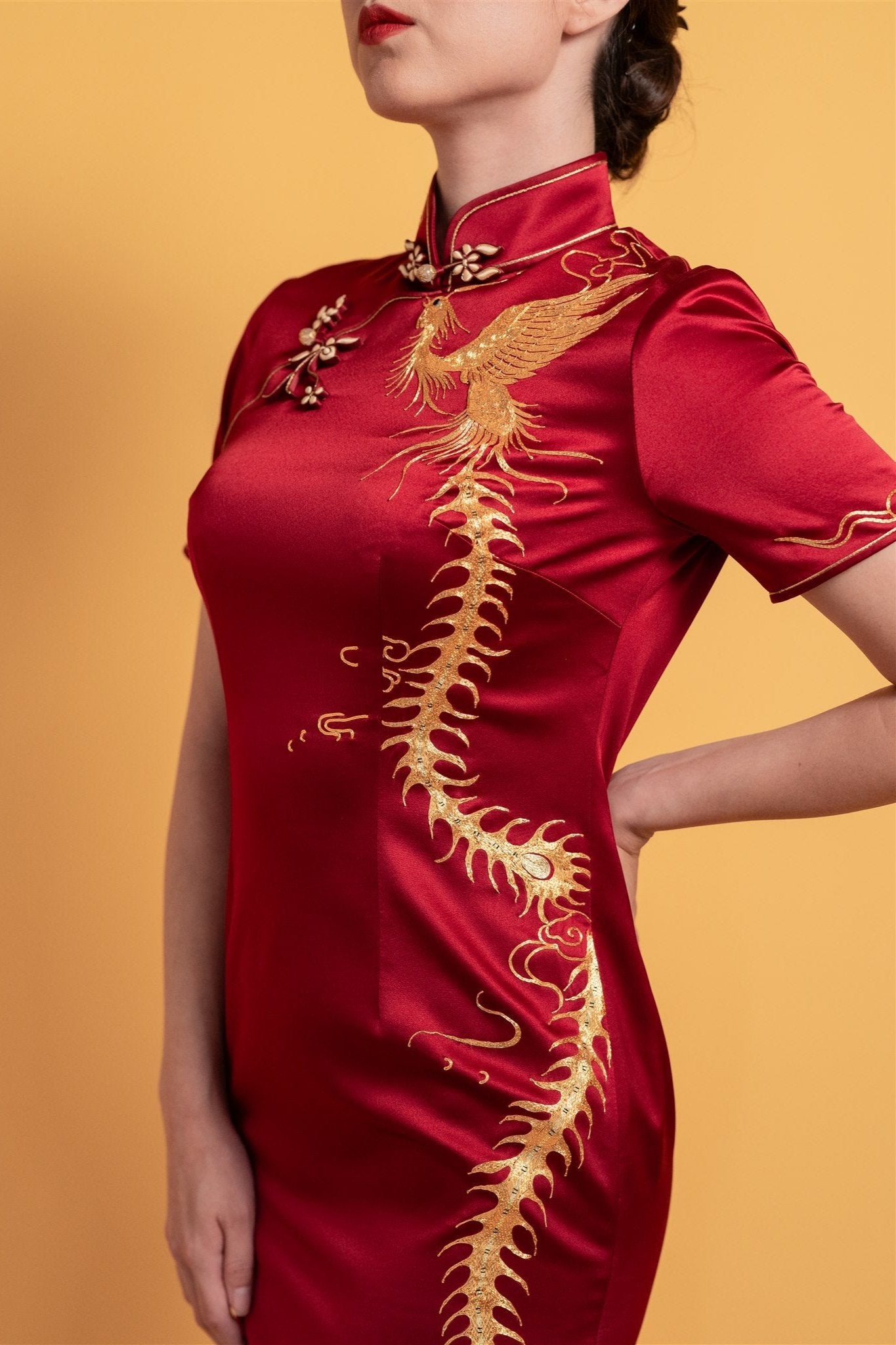 Close-up detail of the gold phoenix embroidery and floral Pankou knot buttons on a wine red silk classic wedding Qipao with a mandarin collar.