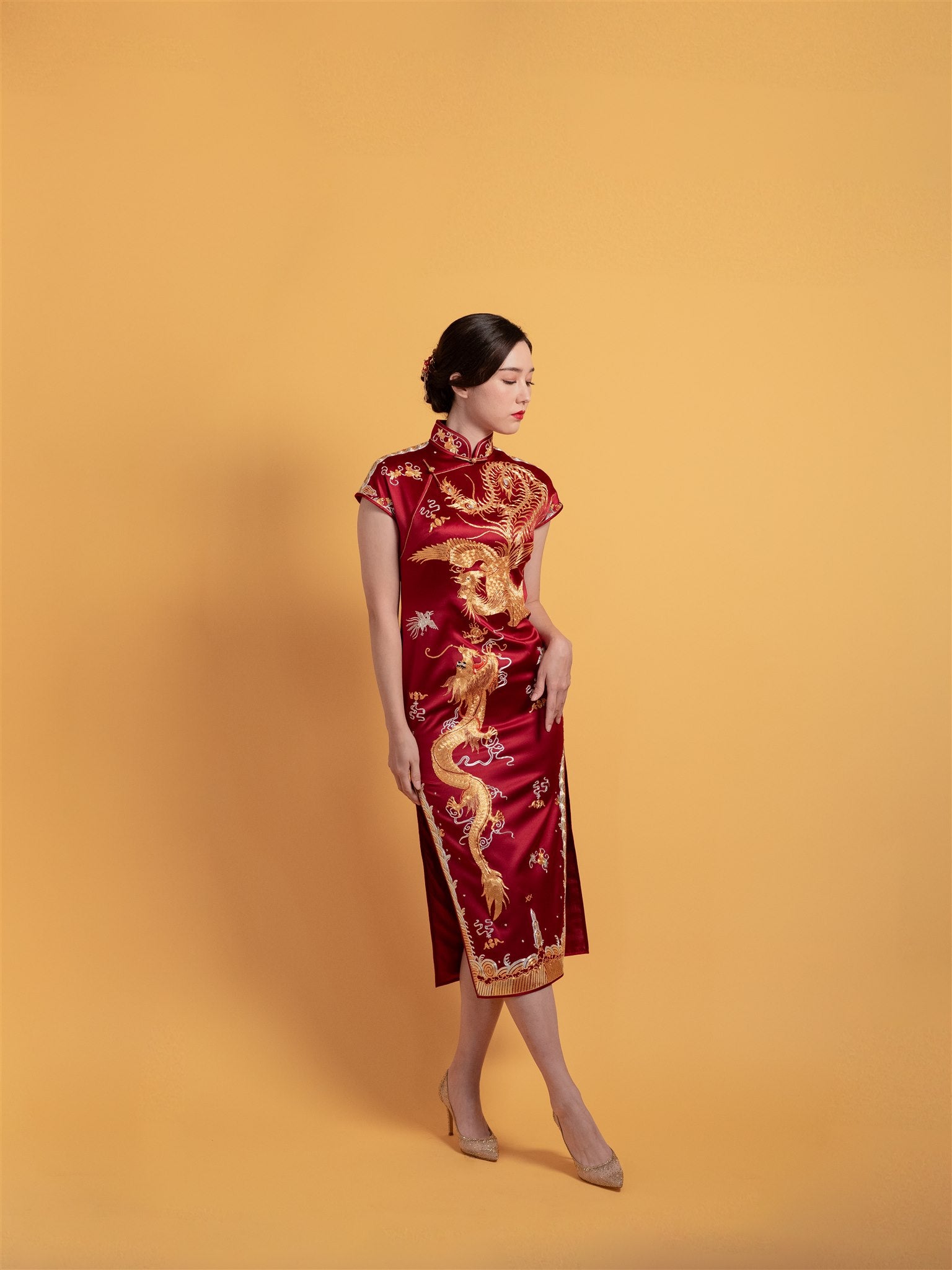 Front view of a wine red silk Qipao dress featuring gold embroidered dragon and phoenix, mid-calf length with cap sleeves, a luxurious piece for weddings.