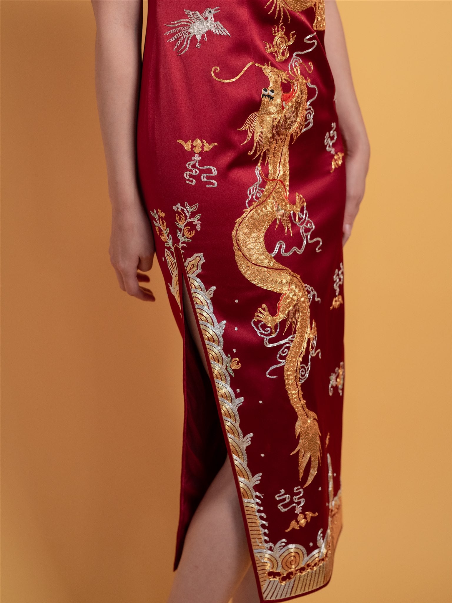 Close-up detail of the skirt of gold dragon embroidery on a wine red silk Qipao dress, mid-calf length with cap sleeves, perfect for a luxurious wedding look.