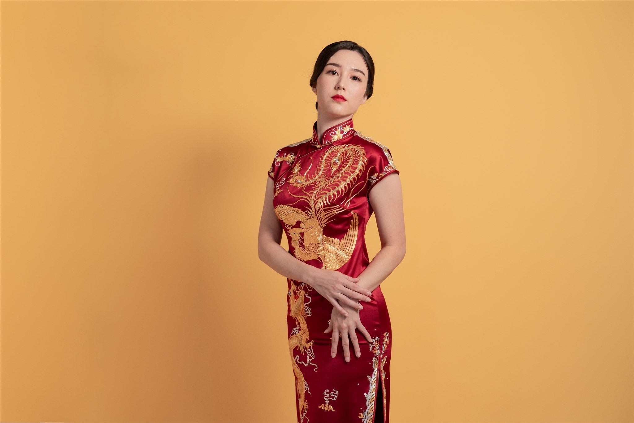 Side view of a wine red silk Qipao dress with intricate gold dragon and phoenix embroidery, mid-calf length and cap sleeves, designed for weddings.