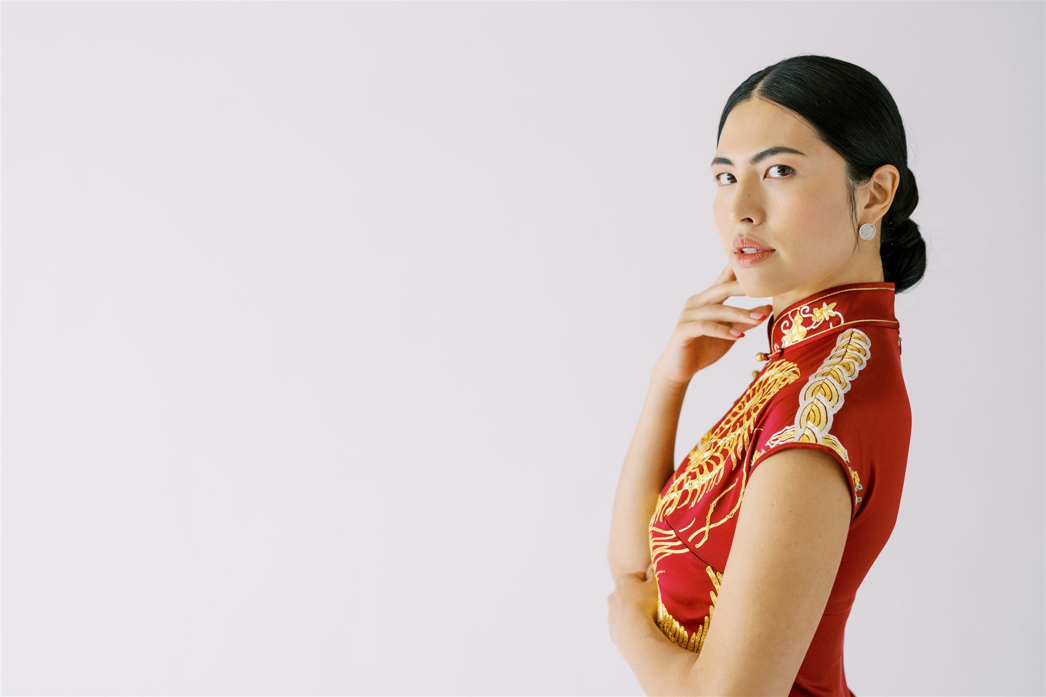 A woman wearing a wine red Qipao with gold embroidered cloud and lotus on the mandarin collar and shoulder