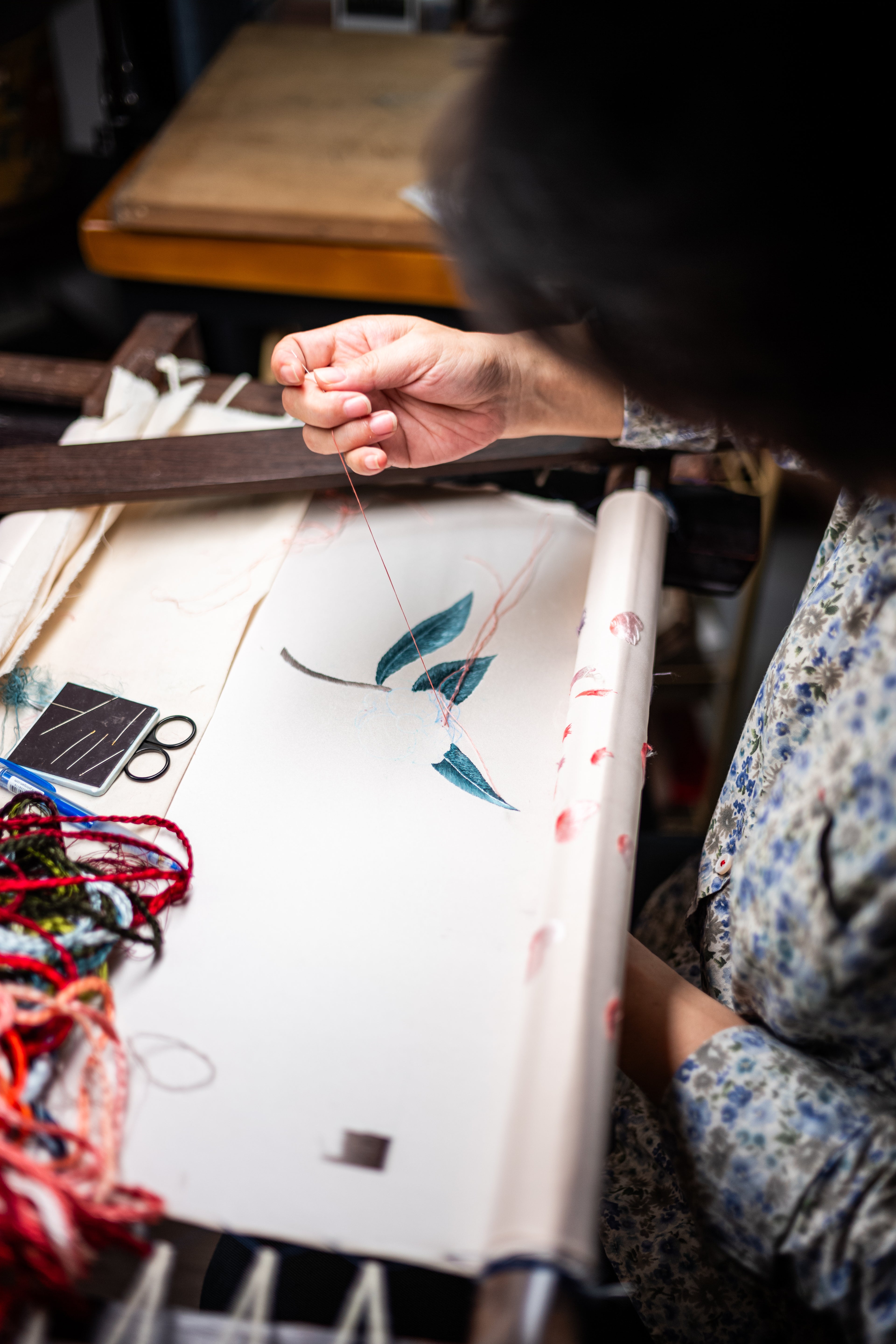 A woman is doing hand embroidery for a custom-made wedding Qipao